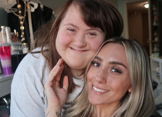 A blonde woman and her sister with Down syndrome smiling.