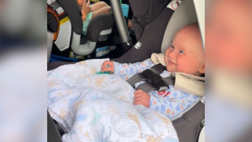 A cute baby sitting in a car seat smiling.