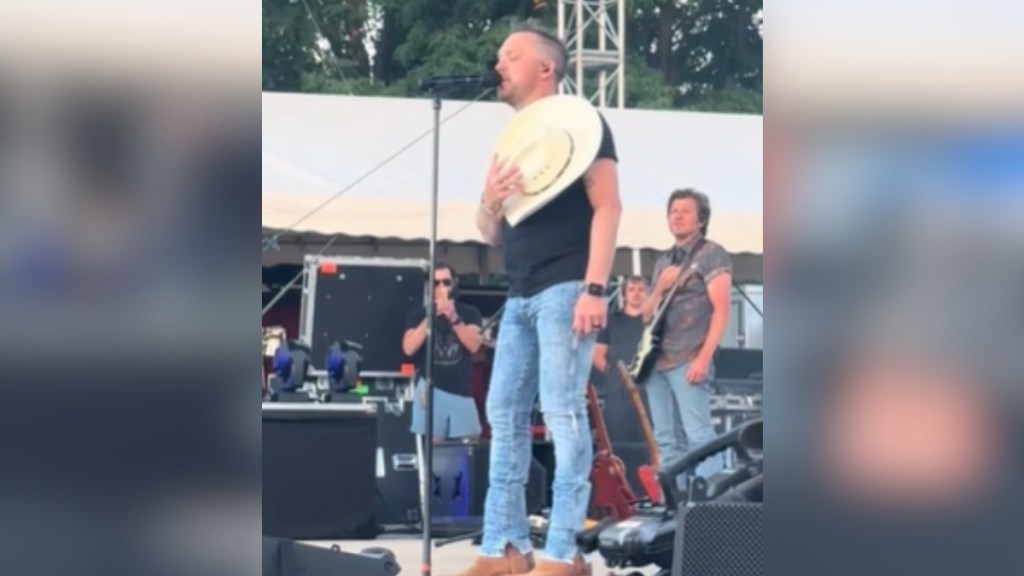 Justin Moore holds his hat across his chest as he sings on stage