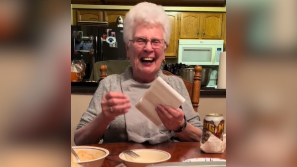 A grandma smiles wide as she sits at a dining table, ultrasound photos in hand.