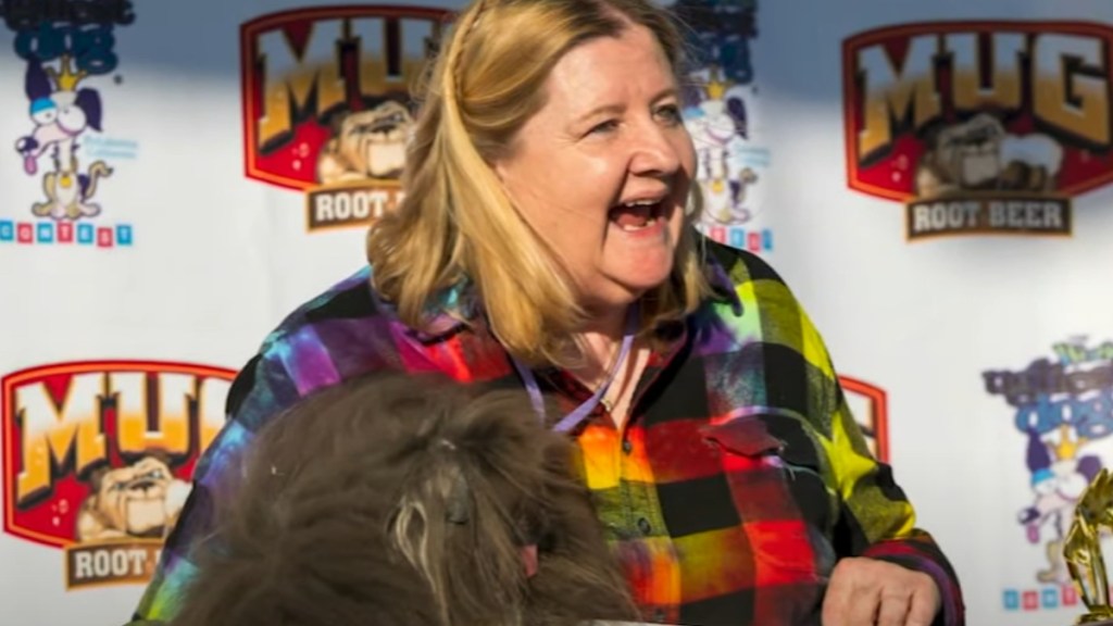 A woman smiles, mouth open, as she holds a tiny dog with lots of fur covering his face.