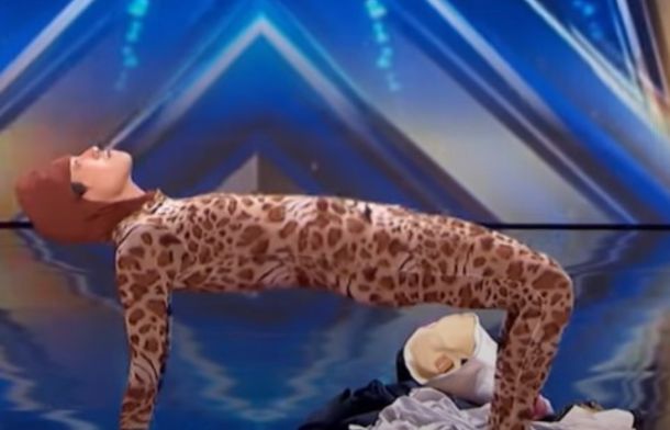 Image shows a man in a spotted one-piece jumpsuit in a crab walk position on the AGT stage.