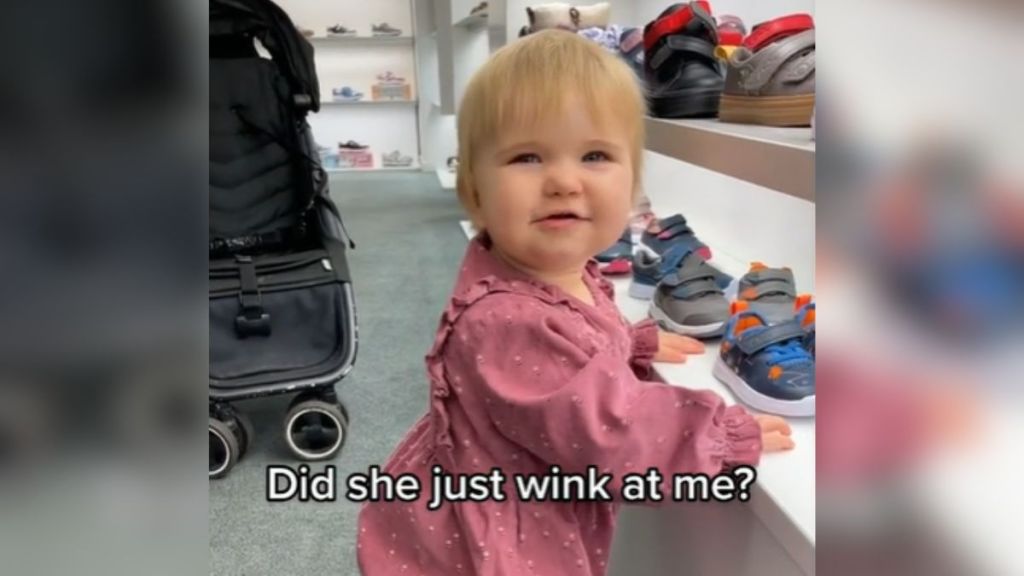 A baby in a pink dress looking up at the camera.