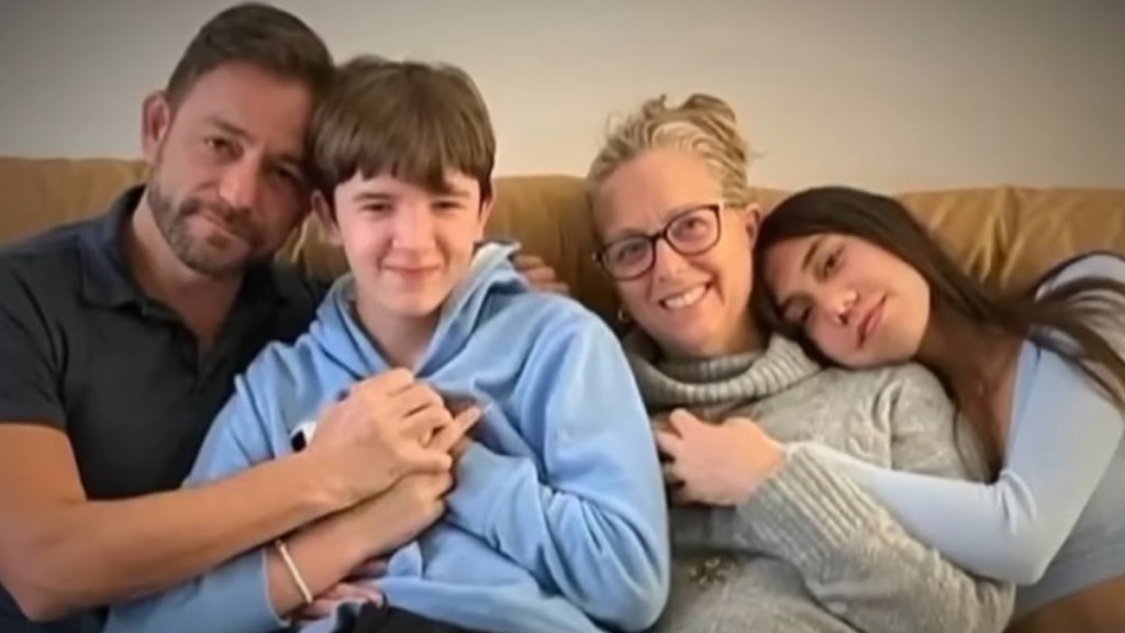 A dad, mom, and their two kids sit close on a couch as they smile and pose for a photo