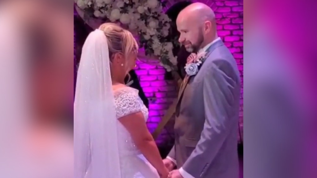A groom and bride hold hands during the wedding ceremony. The bride sings as the groom smiles at her