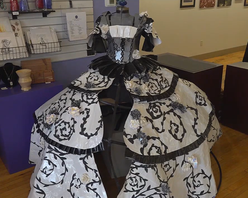 A duct tape dress hangs on a mannequin. It's poofy in the skirt area an is black and white with swirling details in the skirt and arms, which are also poofy.