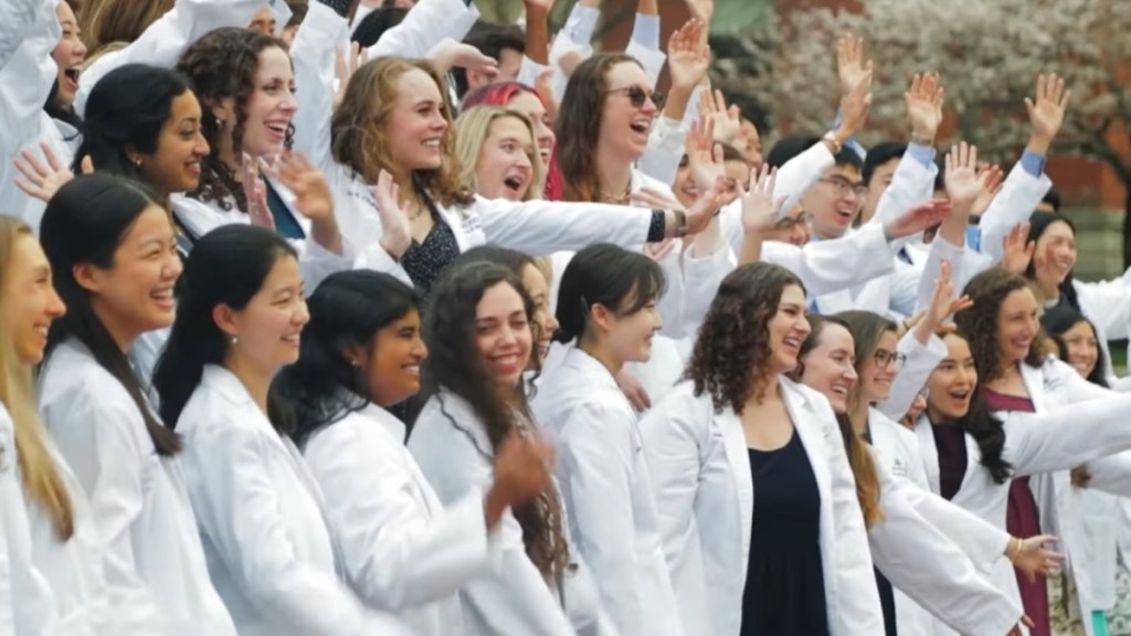 A group of medical students at Johns Hopkins gather together outside, hands raised in the air, cheering over the $1 billion donation to cover tuition