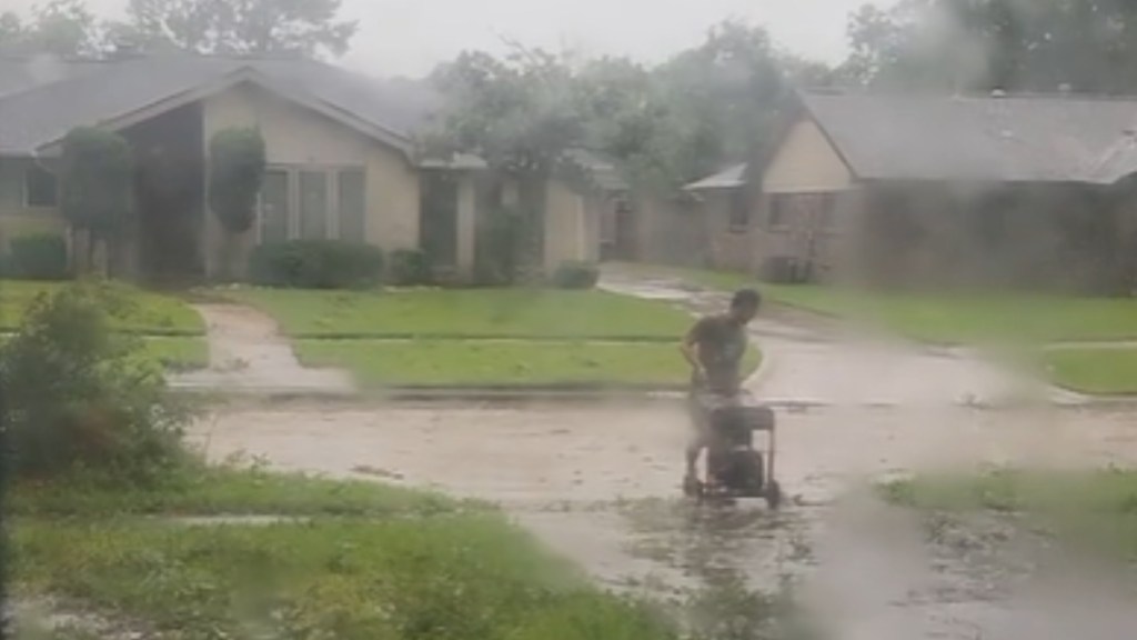 A man pulls a generator down his driveway in the rain