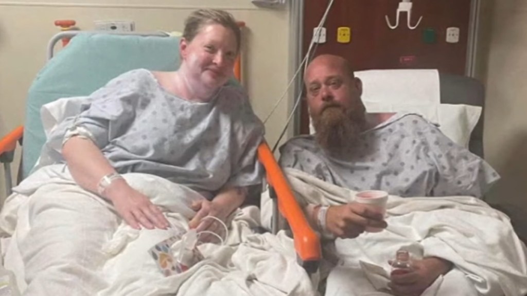 Nathan and Kim in a hospital after their rescue. Kim sits in a bed while Nathan sits in a chair right next to each other.