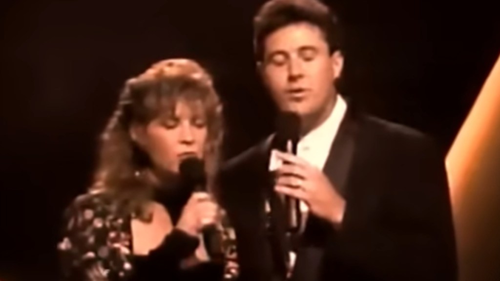 Close up of Patty Loveless and Vince Gill singing into mics, eyes closed