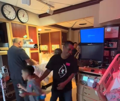A man standing in a hospital room with his family.
