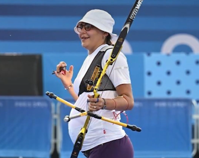 Olympic archer Yaylagul Ramazanova smiles as she looks off at something in the distance as she holds her bow.