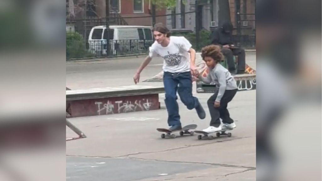 A teenager holding hands with a little boy while both are skateboarding.
