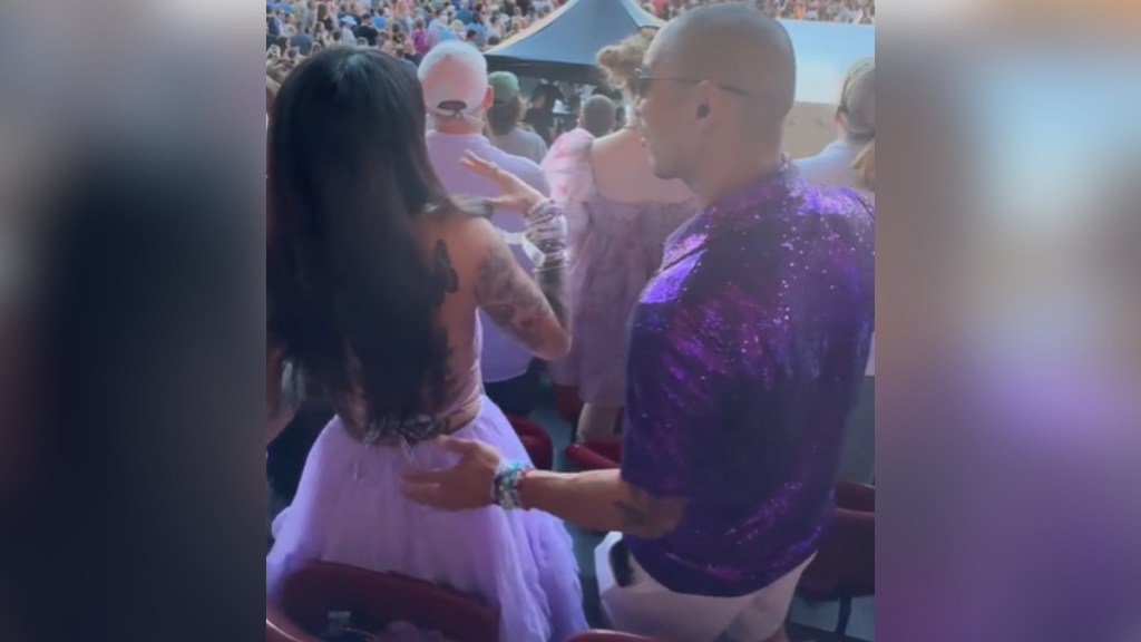 View from behind of two people standing and dancing at a concert. The woman is looking at the stage while the man is slightly turning toward her, arm reaching for around her waist