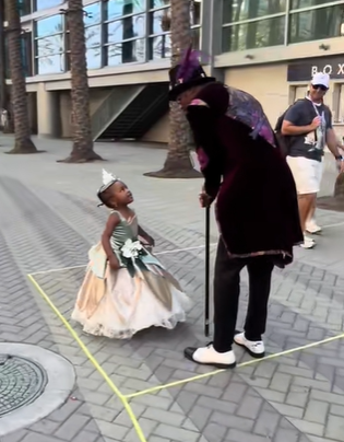 A little girl dressed as Princess Tiana meets a Dr. Facilier cosplayer.