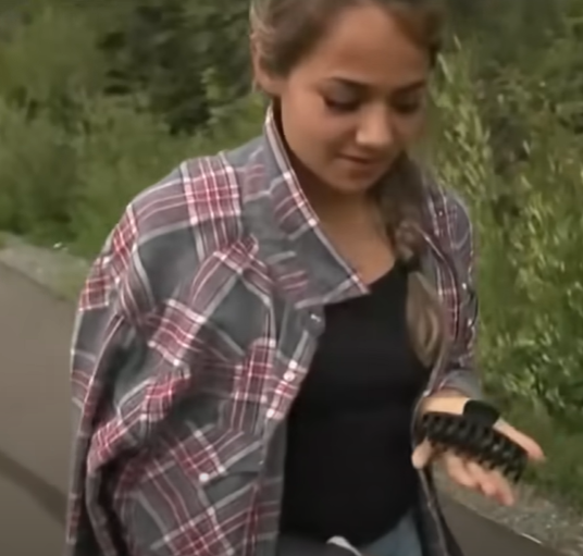 A woman outdoors holding a large hair clip in her hand.