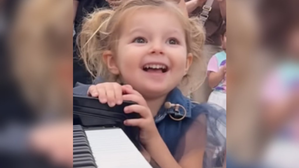 Close up of a smiling 3-year-old girl as she rests her hands on a piano