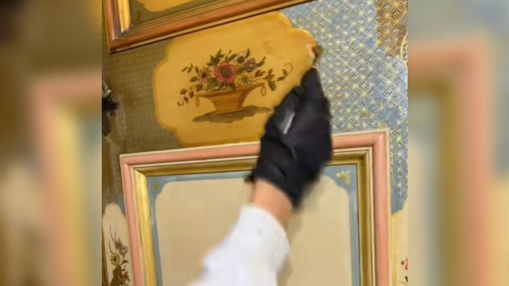 Close up of a yellowed decorative wall panel being restored by someone wearing a glove who is holding a brush