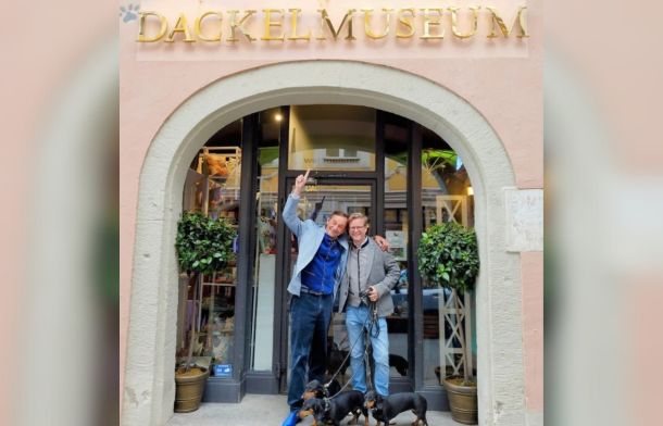 Image shows the entrance to the Dackel Museum with the two founders and their dogs.