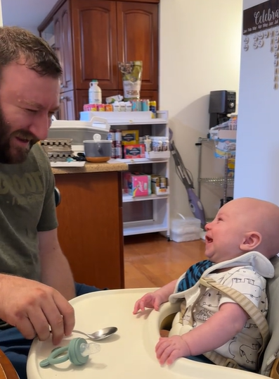 A baby in a high chair laughing with his dad.