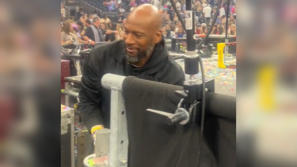 A security guard smiles as he stands partially hidden behind something. It looks like he's grabbing something that can't be seen in this image