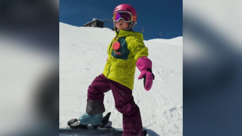 A little girl dons skiing gear as she stands on a slope