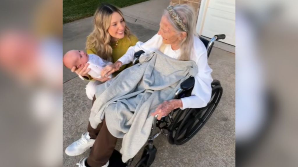 A young woman holding her baby next to her grandma's wheelchair.