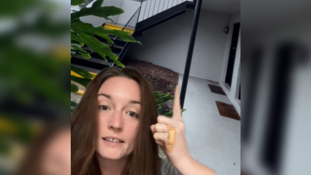 Using a green screen feature on TikTok, a woman talks as she points up near an apartment door. It's a unit on the ground with upstairs neighbors. The door is tucked behind an exterior staircase