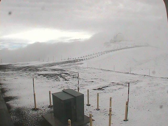 View of a snowy area on Mauna Kea in Hawaii. A road is dusted covered in snow and ice and the mountains in the distance are nearly impossible to see through fog and snow
