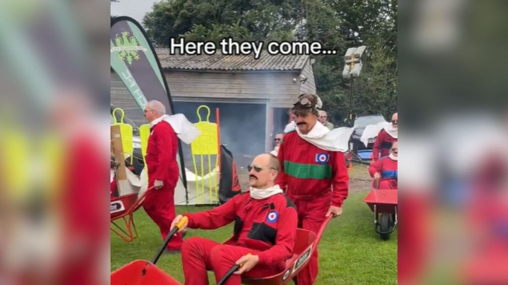 People in red suits pushing each other around in wheelbarrows.
