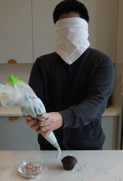 A blindfolded person decorating a cupcake.