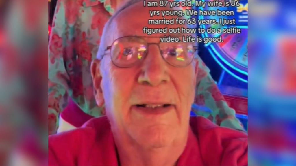 An elderly man with glasses in an arcade with colorful lights.