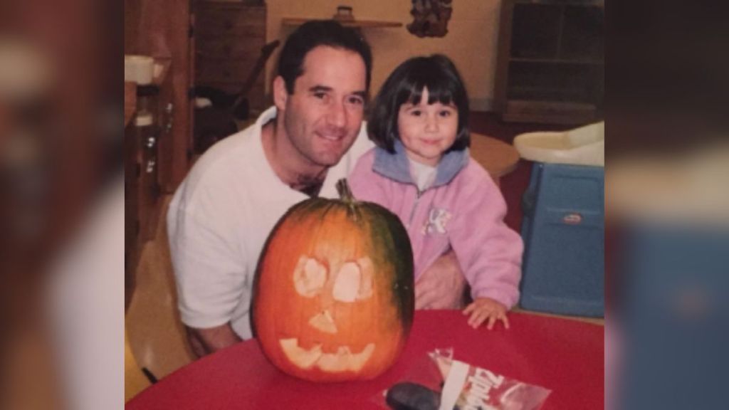 A man and his daughter posing with their jack-o'-lantern.