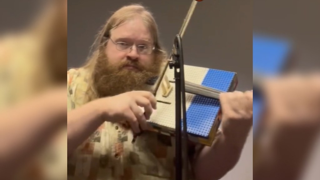 A man plays a LEGO violin as he looks into the camera