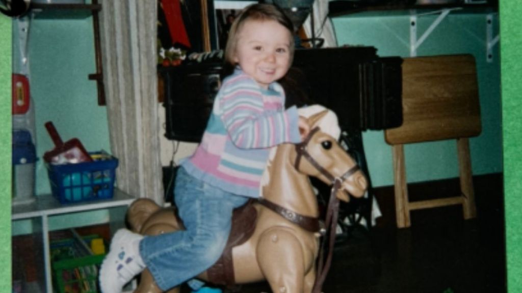 An old photo of a little girl riding a toy horse.