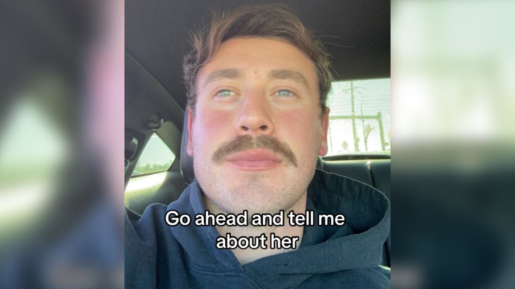 A man takes a selfie in the car. He looks away from the camera and at something in the distance. Text on the image reads: Go ahead and tell me about her
