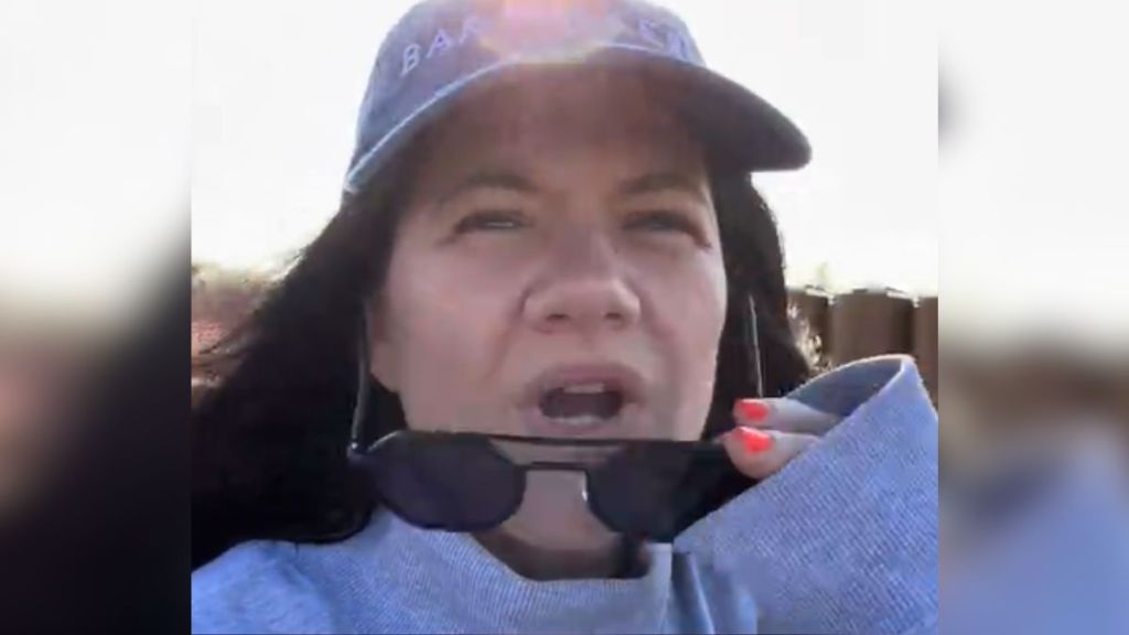 A woman lowering her sunglasses and squinting.