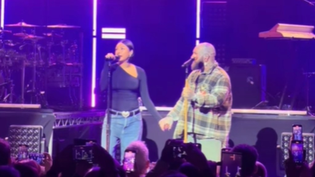 Raiche Wright and Teddy Swims sing into two different mics on stands. They hold each other's hands as they do