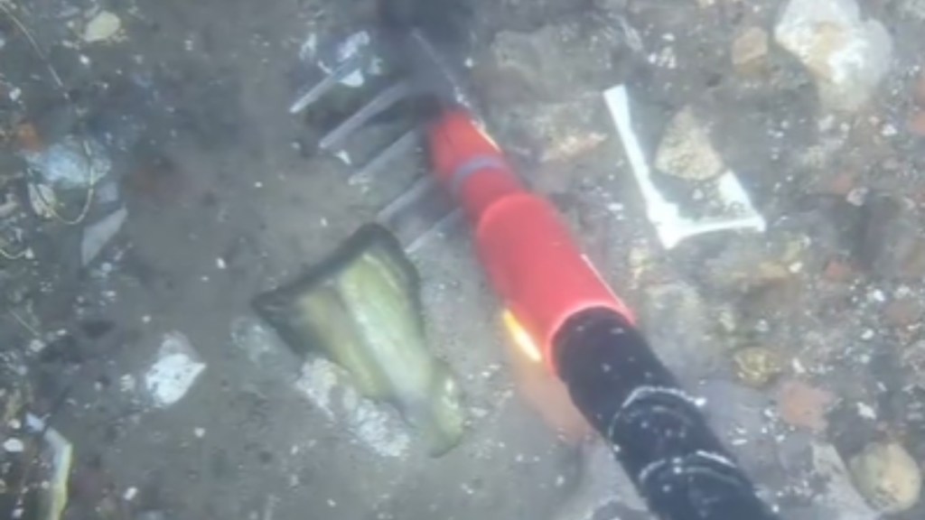 View of a long tool being used to dig up an object that is half-buried at the bottom of a river