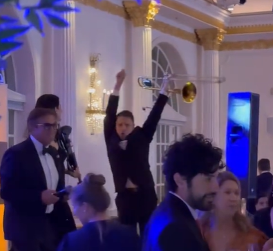 A trombone player dancing on stage at a wedding reception.