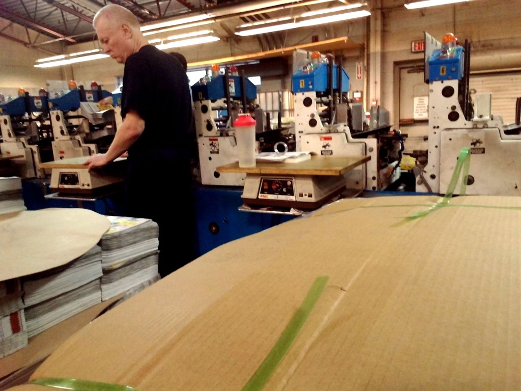 View from the side of a man, Ed, as he does work at an insertion machine for newspapers. 
