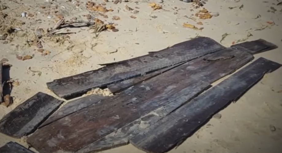 Broken-up pieces of a coffin are laid out on a beach