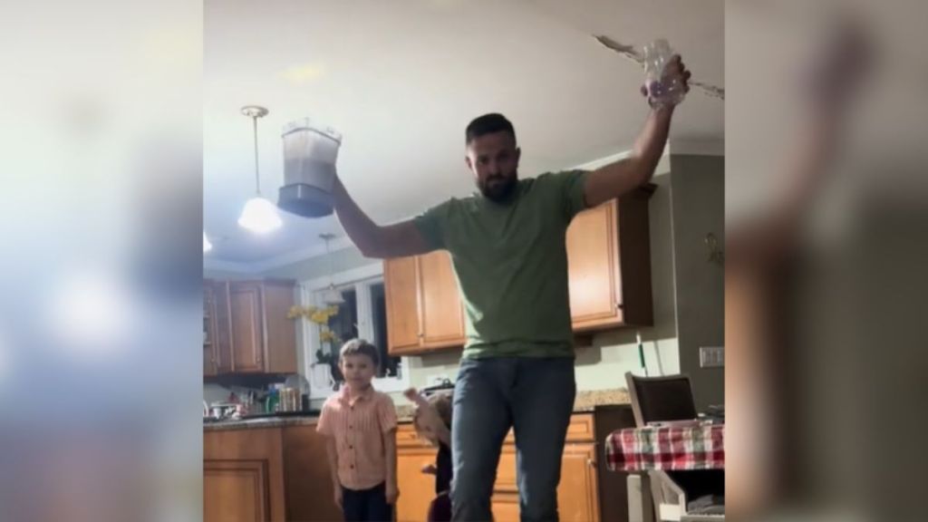 A man holding a blender in one hand and a cup in another while his kids stand behind him.