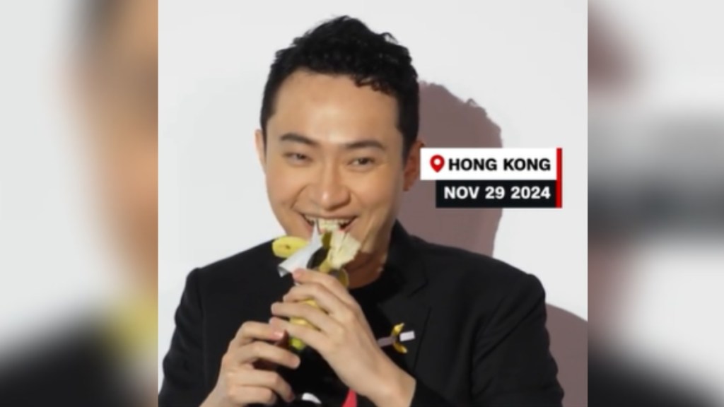 Close up of Justin Sun as he starts to take a bite of a banana from the art piece "Comedian." Text on the image reads Hong Kong. Nov. 29 2024