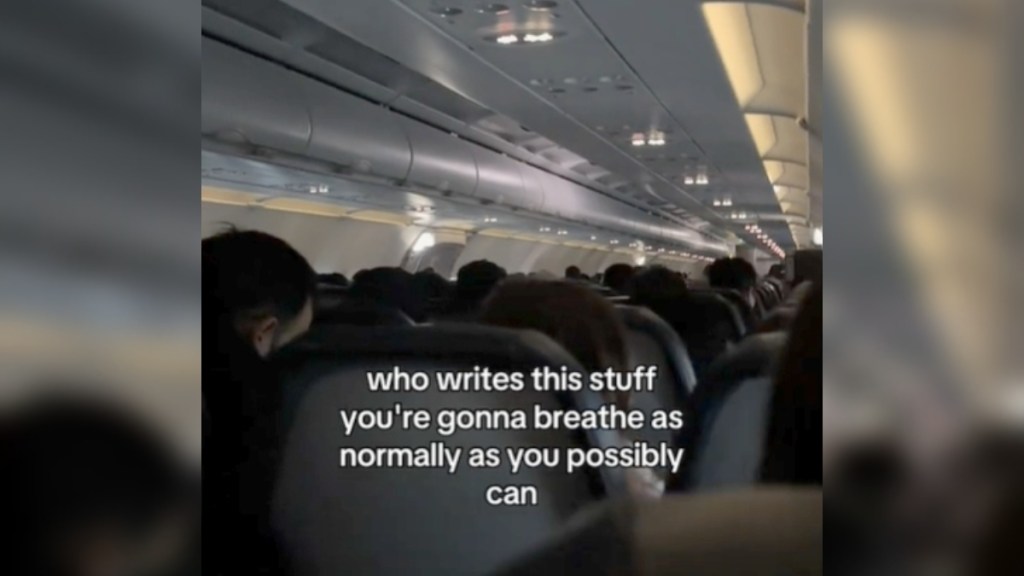 View from the seat on an airplane. There are quite a few people onboard. Text on the image reads: who writes this stuff you're gonna breathe as normally as you possibly can