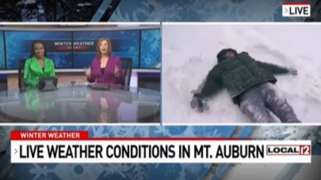 Image shows Bob Herzog making snow angels during a live weather broadcast as inside anchors look on.