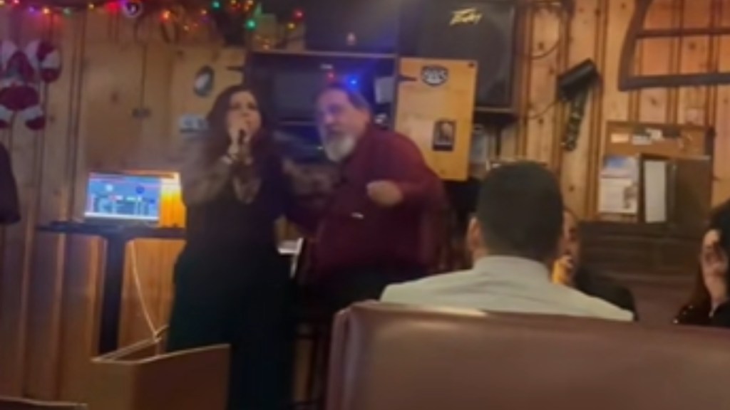 A man and woman passionately sing karaoke to a small crowd at a bar