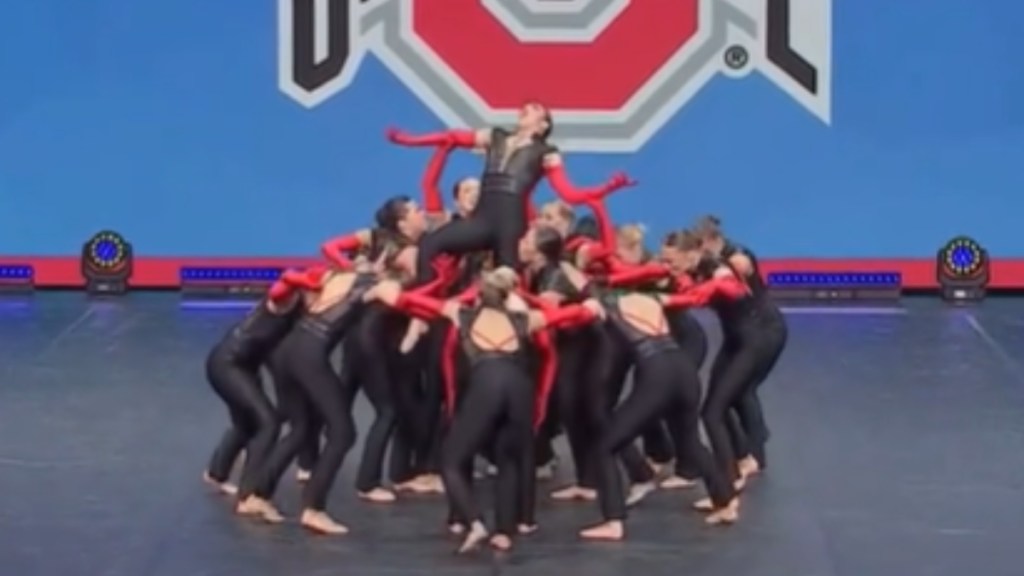 A group of dancers gather in a circle, lifting a single dancer above them. This single dancer holds out her arms and holds her head back, seemingly screaming