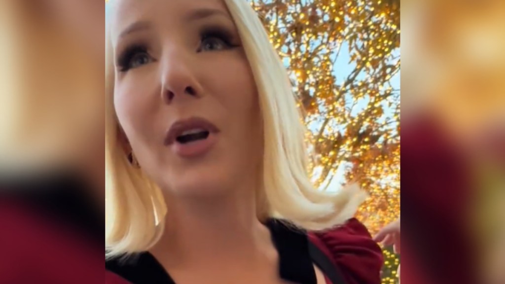 Close up of a blonde woman as she walks and talks outside. She has a shocked look on her face as she looks in the distance at something that can't be seen in this image