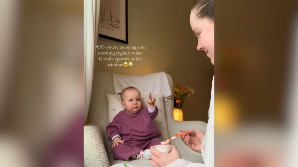 A baby pointing at something in the distance while Mom feeds her.
